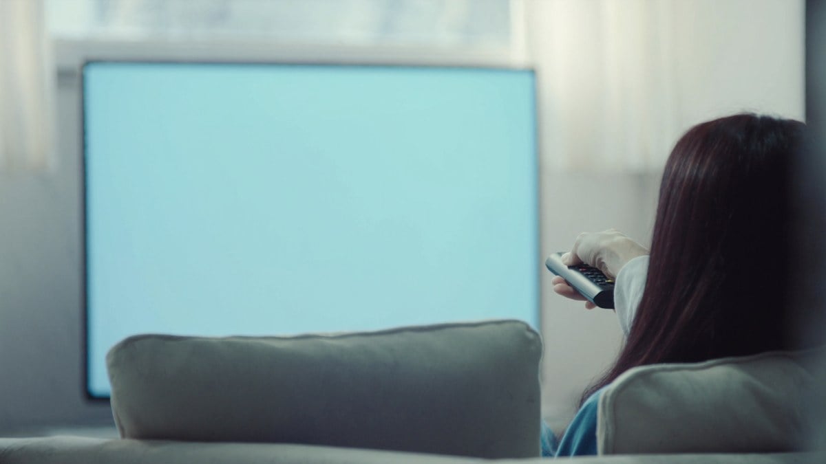 소파에서 리모컨을 들고 멈춘 TV 화면을 보는 여성