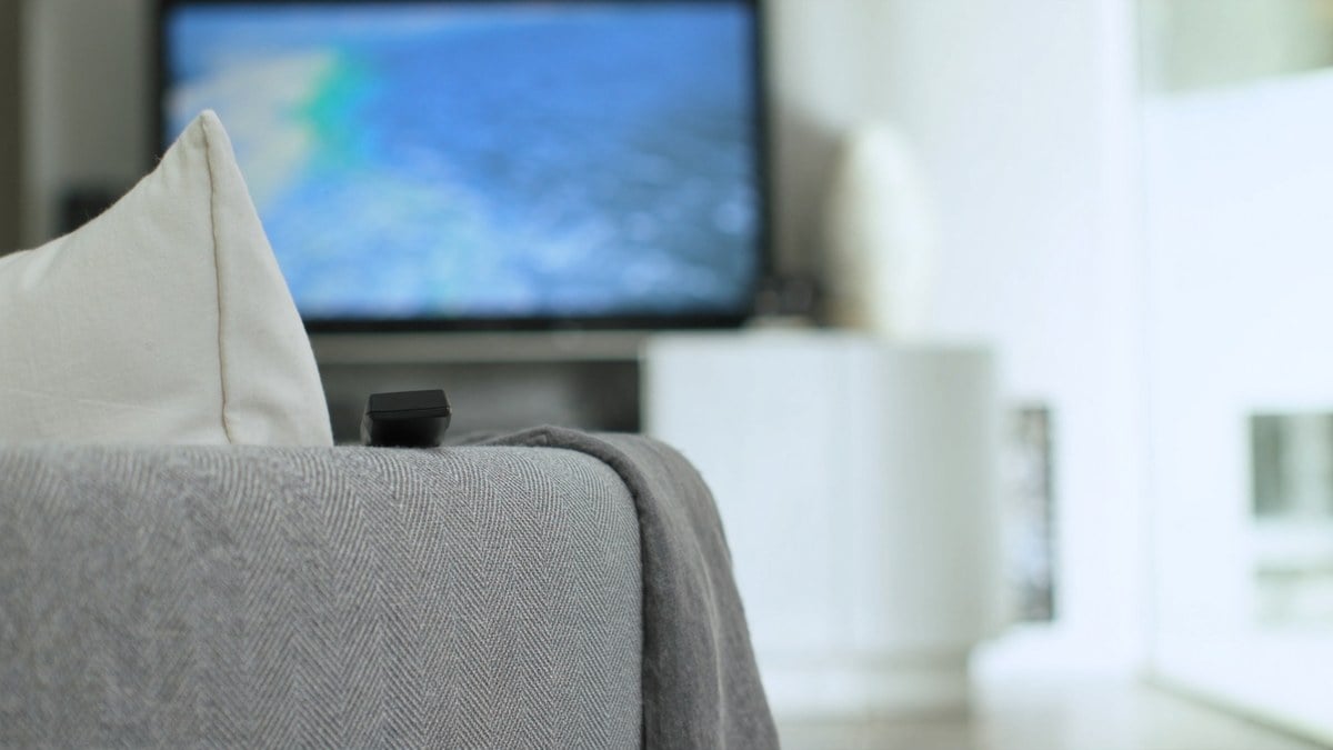 소파 팔걸이의 리모컨과 바다 풍경이 흐리게 보이는 TV