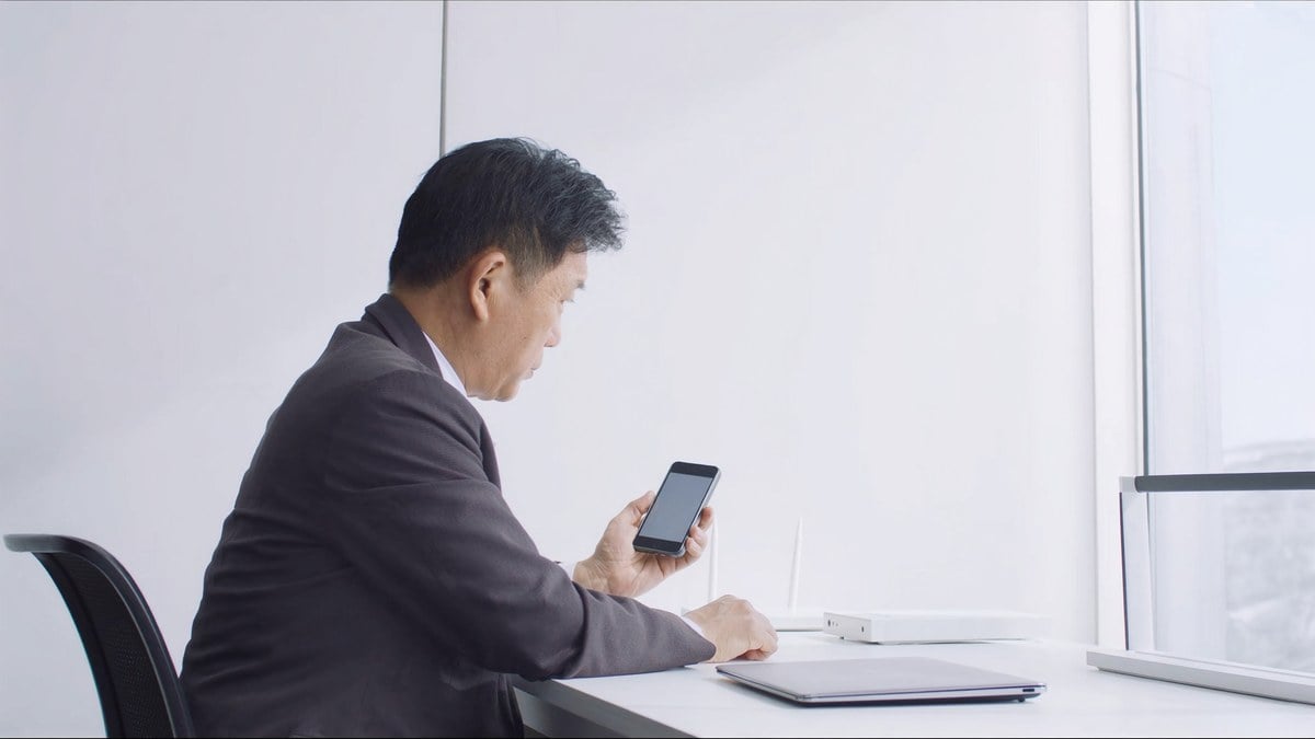 책상에서 휴대폰과 공유기를 보며 고민하는 남성