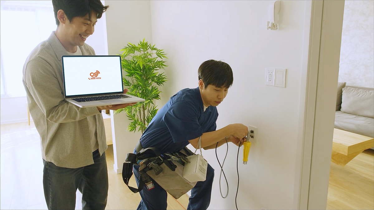 인터넷 설치 기사가 벽 단자에 선을 연결하고 집주인이 노트북을 들고 지켜보는 모습