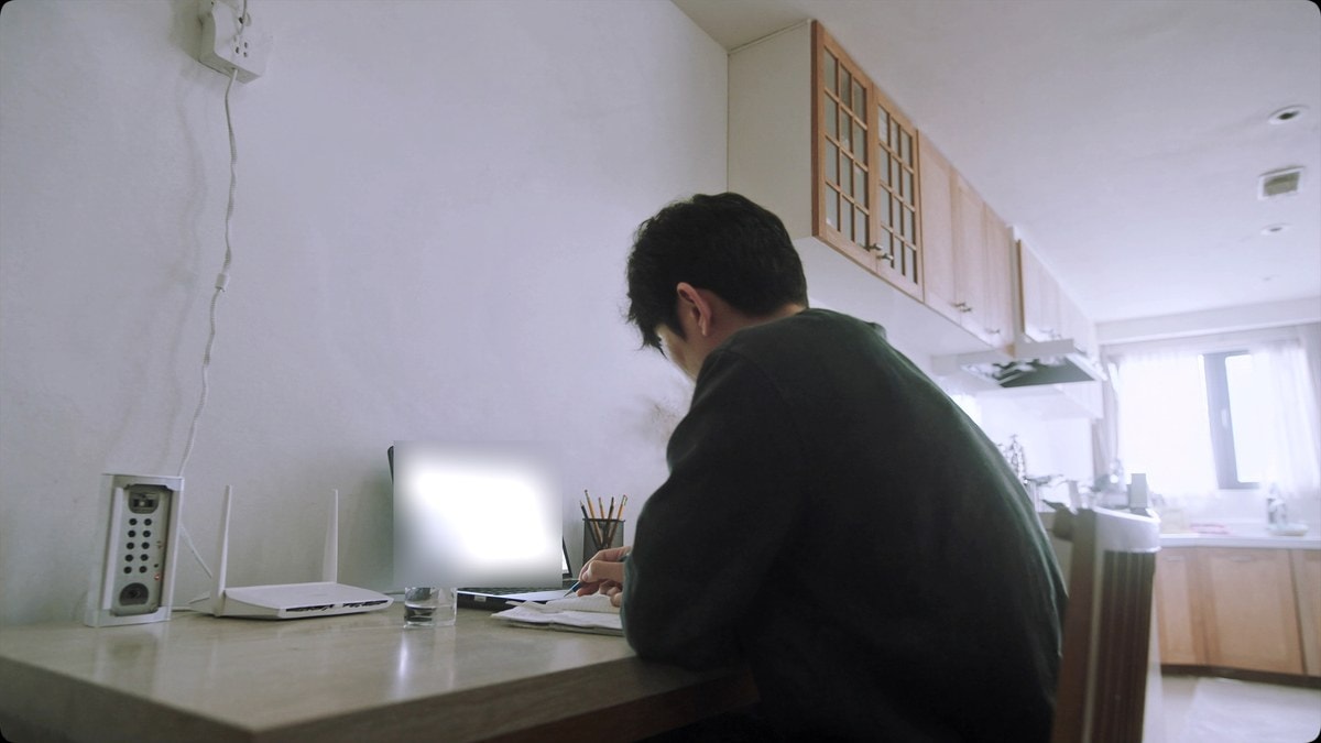 책상에서 노트에 계산을 적는 남성과 노트북, 공유기
